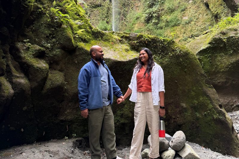 Bhavana and Akash holding hands in front of a waterfall